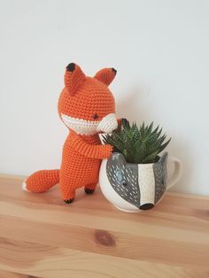 a crocheted fox sitting next to a potted plant on a wooden table