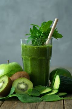 a green smoothie with kiwis, mint and leaves on a wooden table