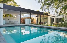 a swimming pool in front of a house with glass walls and sliding doors on the side