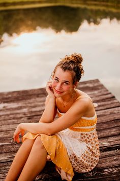 a woman sitting on a dock next to a body of water with her hand under her chin