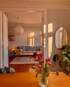 a vase filled with red flowers sitting on top of a wooden table next to a living room