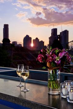 two glasses of wine are sitting on a table with flowers in front of the city skyline