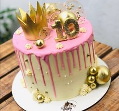 a birthday cake decorated with gold and pink icing on a wooden table next to other decorations