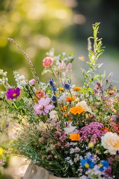 an arrangement of wildflowers and other flowers in a wooden bucket on the ground