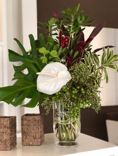 a vase filled with flowers and greenery on top of a table