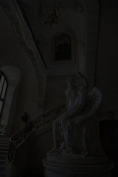 a statue sitting on top of a white pedestal next to a stair case in a building