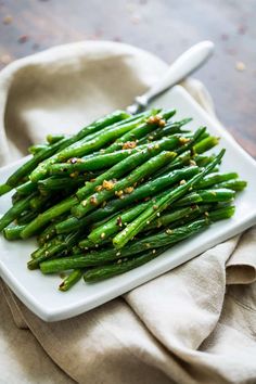 asparagus with sesame seeds and seasoning on a white plate next to a napkin