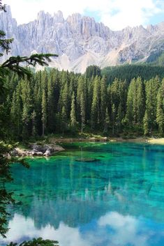 a lake surrounded by trees and mountains with blue water in the foreground on a sunny day