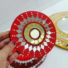 a person holding a red and yellow plate with designs on it next to another plate