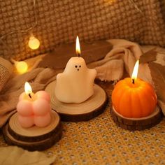 three candles are sitting on wood slices with small pumpkins in the middle and one candle is lit