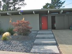 a house with red door and steps leading up to the front entrance, surrounded by gravel