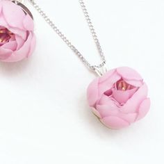 two pink flowers are hanging from a silver chain on a white surface with one flower in the center