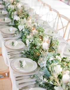 a long table with white plates and greenery