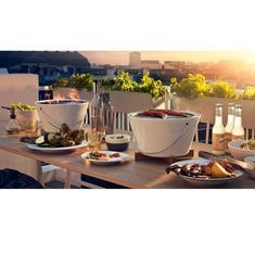 a wooden table topped with bowls and plates of food next to a fire pit on top of a roof