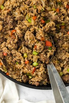 a skillet filled with rice and meat on top of a white cloth next to two spoons