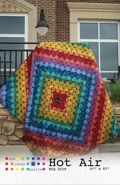 a multicolored quilt sitting on top of a stone wall next to a brick building