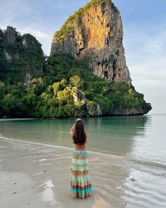 a woman standing on top of a sandy beach next to the ocean with a mountain in the background