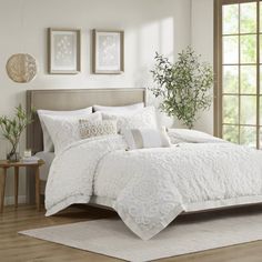 a bed with white comforter and pillows in a room next to a large window