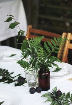 the table is set with two vases filled with leaves and berries, along with an empty glass bottle