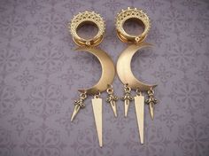 two pairs of gold toned earrings with spikes and chains hanging from the sides, on a purple background