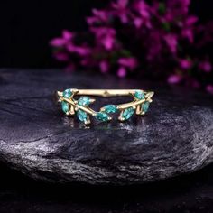 an image of a gold ring with green stones on the side and purple flowers in the background