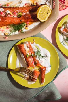 two yellow plates with food on them next to a platter of fish and lemon wedges