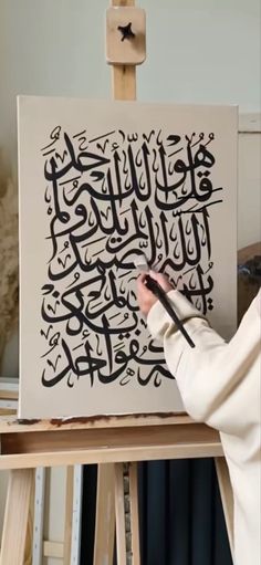 a person is painting on a canvas with black letters in arabic and islamic scripts