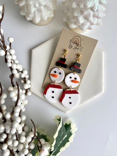 the snowman earrings are on display next to some white flowers