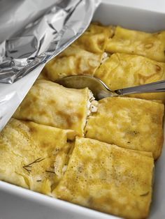 some food is in a white dish with silver foil on the side and a spoon next to it