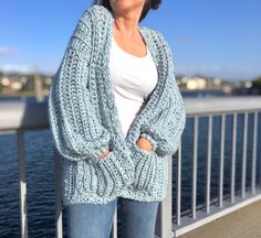 a woman standing on a bridge wearing a blue knitted cardigan and smiling at the camera