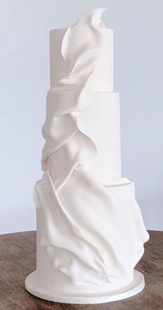 a three tiered white wedding cake with ruffles on the top and bottom