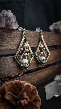 two earrings with skulls and flowers on them sitting on top of a piece of wood