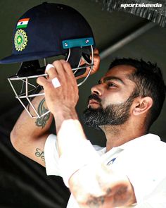 a man with a beard holding a cricket helmet up to his face while wearing a white shirt