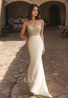 a woman in a long white dress standing on a cobblestone walkway with her hand on her hip