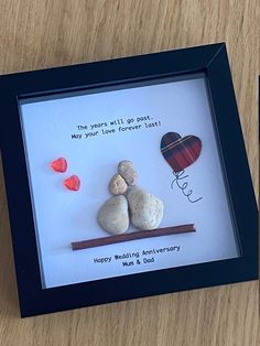 two rocks in a shadow frame on a wooden table next to a greeting card with the words happy wedding anniversary