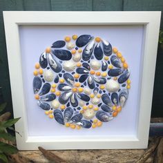 a white frame holding a blue and yellow art work with shells on it's surface