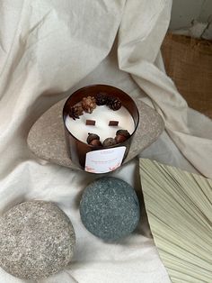 a candle and some rocks on a white cloth next to a basket with pine cones