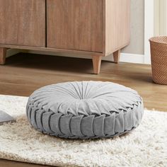 a round dog bed sitting on top of a white rug next to a wooden cabinet