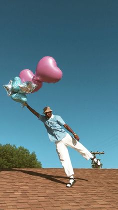 a man standing on top of a roof holding onto two large pink heart shaped balloons