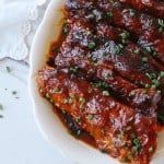 a white plate topped with ribs covered in sauce and garnished with green onions