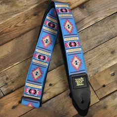 a blue camera strap with an embroidered design on the front and back side, sitting on a wooden floor