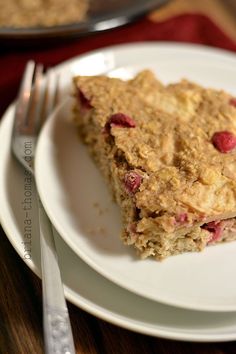 a white plate topped with a piece of cake on top of a wooden table next to a fork