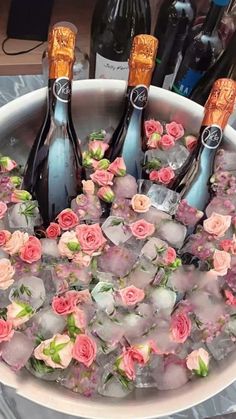 four bottles of champagne are in an ice bucket with pink flowers and roses on it