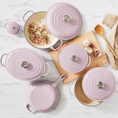 purple pots and pans on a white marble counter top with wooden cutting board, utensils and spoons