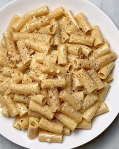 a white plate topped with pasta and seasoning on top of a marble countertop