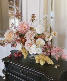 a vase filled with flowers sitting on top of a black dresser next to a mirror