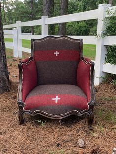 an old chair with a cross on it sitting in the grass next to a fence