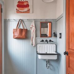 a white sink sitting under a painting next to a wooden door with a brown bag hanging on the wall