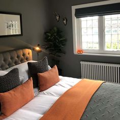 a bed with orange and gray pillows next to a white radiator in front of a window