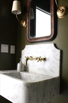 a bathroom sink sitting under a mirror next to a wall mounted faucet and light fixture